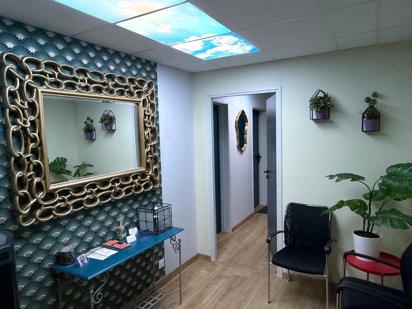 Vue de la salle d’attente partagée, avec sièges, plantes et console bleue.